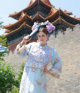 hanfu photoshoot, the forbidden city, beijing, qing dynasty, female, solo, chinatrip, Woman in a pale blue embroidered dress with a floral crown holds a scroll, posing before a tiered Chinese temple roofed in orange tiles.