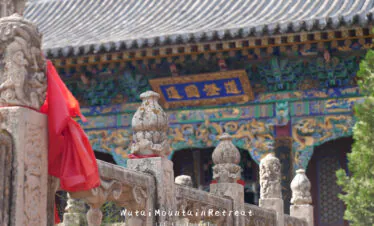wutai retreat, shanxi, chinatrip, Stone carved balusters in a temple courtyard with a colorful, ornate temple facade in the background and red cloth draped on the railing.