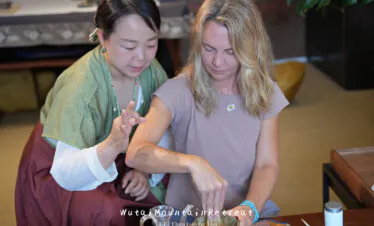 wutai retreat, shanxi, chinatrip, Two women participate in a tea ceremony; one guides the other as they whisk tea powder in a bowl together in a cozy setting.