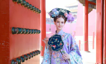 hanfu photoshoot, the forbidden city, beijing, qing dynasty, female, solo, chinatravel, Woman in a lavender traditional Chinese dress with a floral headdress posing beside a red ornate gate.