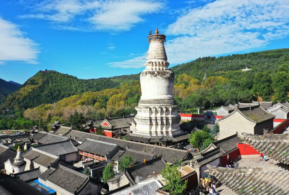 Mount Wutai, shanxi, china, china tour, White Buddhist stupa rising above a Chinese temple complex with gray tiled roofs and green hills in the background.