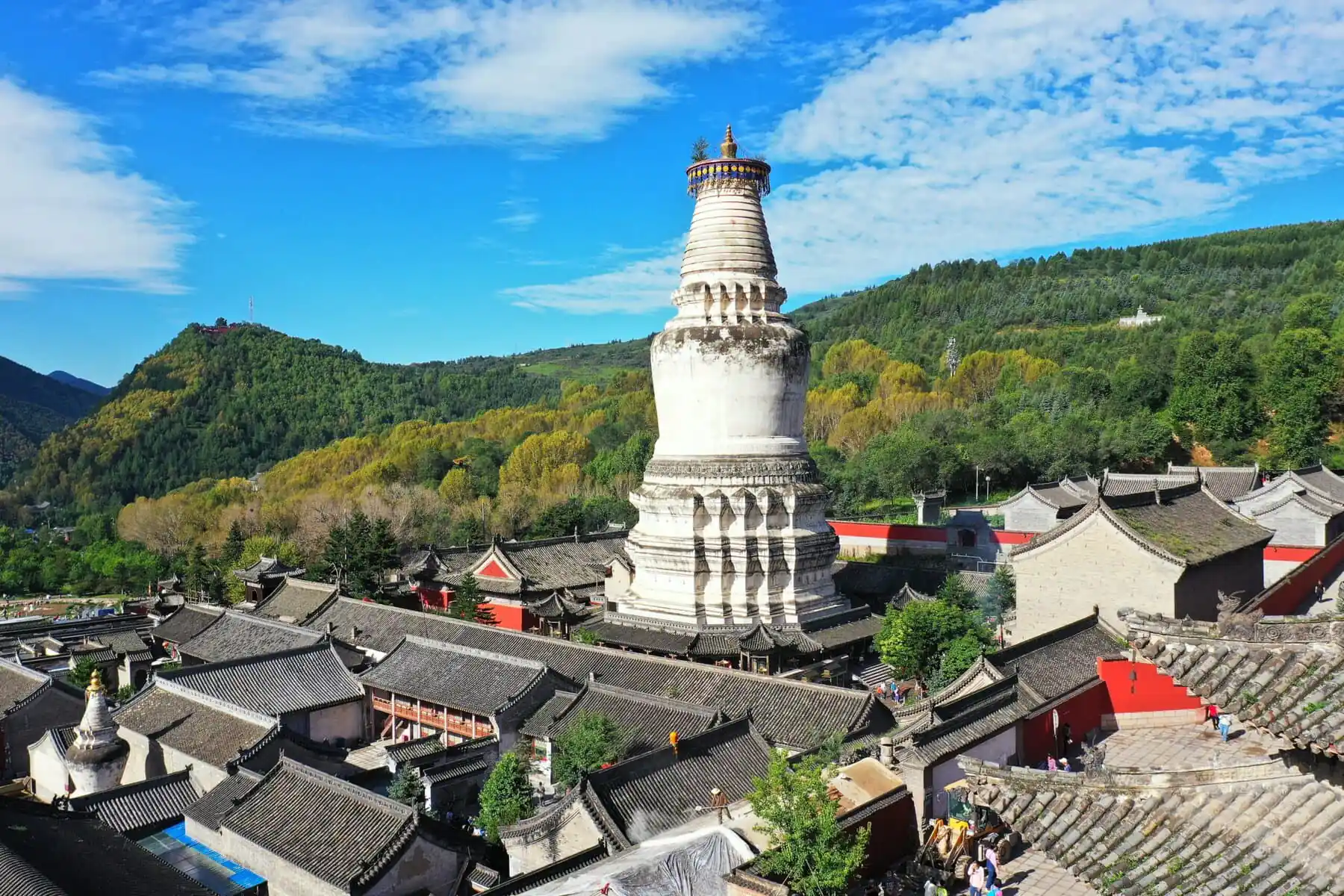 Mount Wutai, shanxi, china, china tour, White Buddhist stupa rising above a Chinese temple complex with gray tiled roofs and green hills in the background.