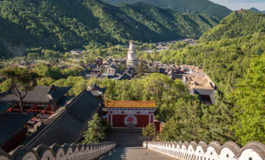 Foguang Temple, Mount Wutai, shanxi, china, china tour, Wide view of a traditional Chinese hill town with a white pagoda at center, surrounded by green mountains and red-tiled roofs.