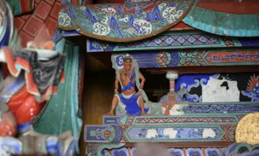 Foguang Temple, Mount Wutai, shanxi, china, china tour, Stacked, ornately painted wooden panels from a temple or shrine, featuring blue, green, and red geometric and wave patterns with a small carved warrior figure in blue and orange standing among them