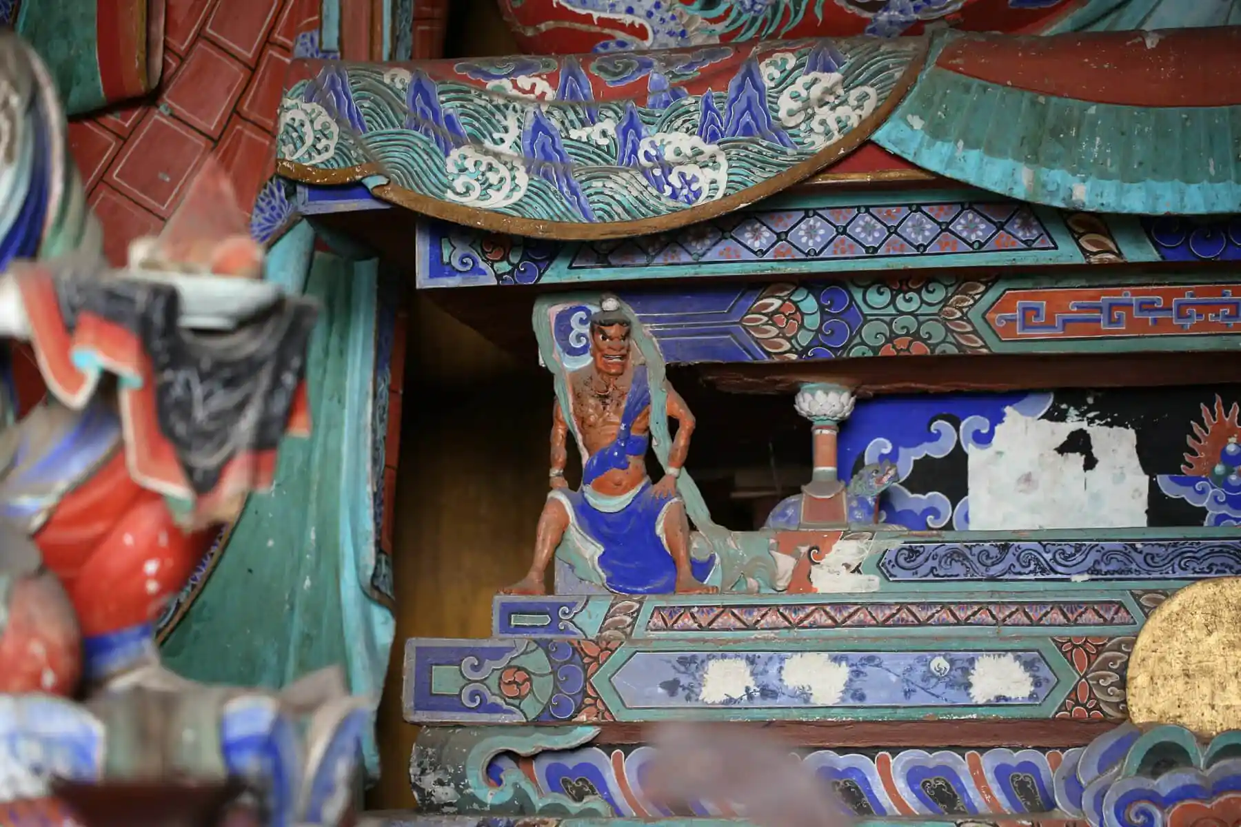 Foguang Temple, Mount Wutai, shanxi, china, china tour, Stacked, ornately painted wooden panels from a temple or shrine, featuring blue, green, and red geometric and wave patterns with a small carved warrior figure in blue and orange standing among them