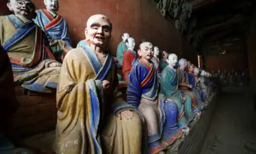 Foguang Temple, Mount Wutai, shanxi, china, china tour, Line of colorful seated Buddhist statues along a wooden wall inside a dim temple, facing forward with robes in yellow, blue, and green.