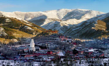 Mount Wutai, shanxi, china, china tour, Snowy mountain town with red buildings and a white pagoda in the foreground, snow-covered slopes in the background under a blue sky.