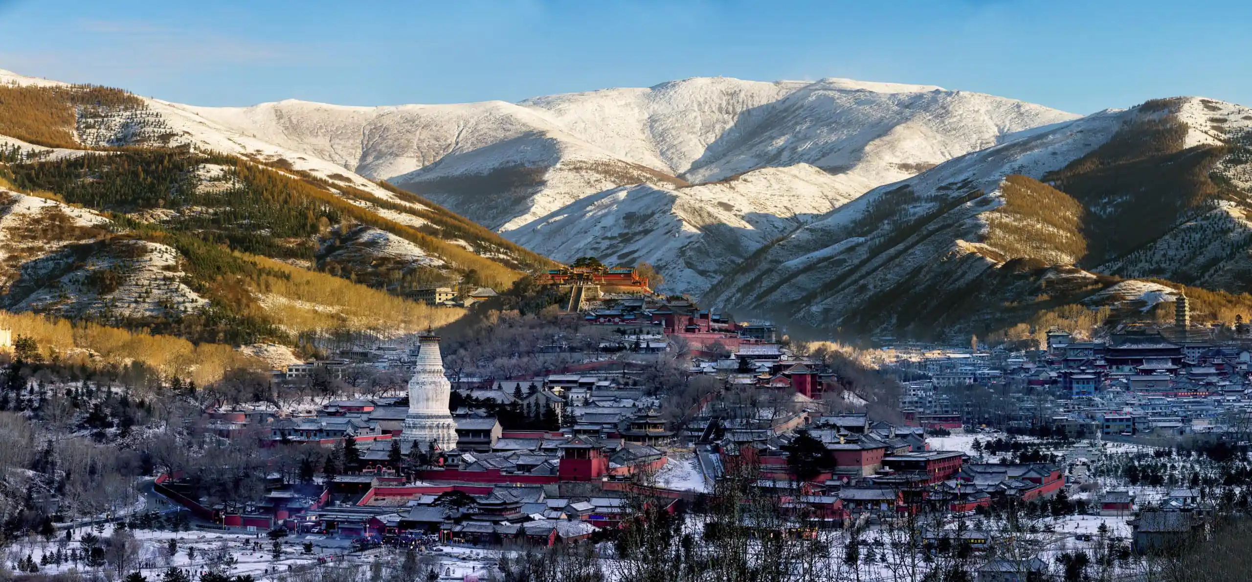 Mount Wutai, shanxi, china, china tour, Snowy mountain town with red buildings and a white pagoda in the foreground, snow-covered slopes in the background under a blue sky.