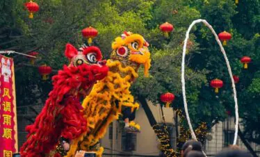 Chinese New Year Adventure jorney, southern china, chinatrip, Two colorful dragon/demon dancers perform a lion-like creature dance with a white hoop in front of a crowd at a festival, red lanterns overhead.