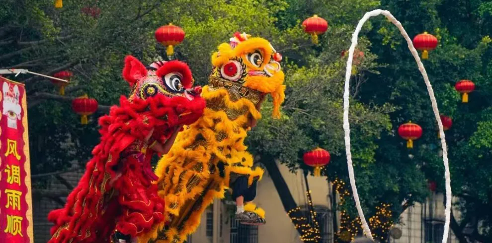 Chinese New Year Adventure jorney, southern china, chinatrip, Two colorful dragon/demon dancers perform a lion-like creature dance with a white hoop in front of a crowd at a festival, red lanterns overhead.