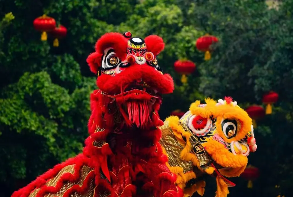 Chinese New Year Adventure jorney, southern china, chinatrip, Two ornate dragon heads, red and yellow, perform a dragon dance in a park with red lanterns overhead.