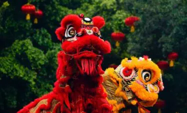 Chinese New Year Adventure jorney, southern china, chinatrip, Two ornate dragon heads, red and yellow, perform a dragon dance in a park with red lanterns overhead.