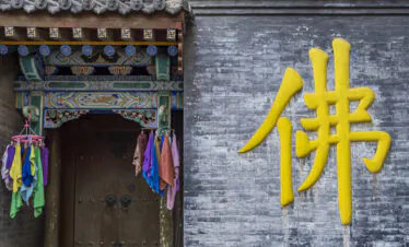Pushou Temple, Mount Wutai, shanxi, china, china tour, Bright yellow Chinese character painted on a weathered gray brick wall beside a richly painted temple doorway with hanging colorful cloths.