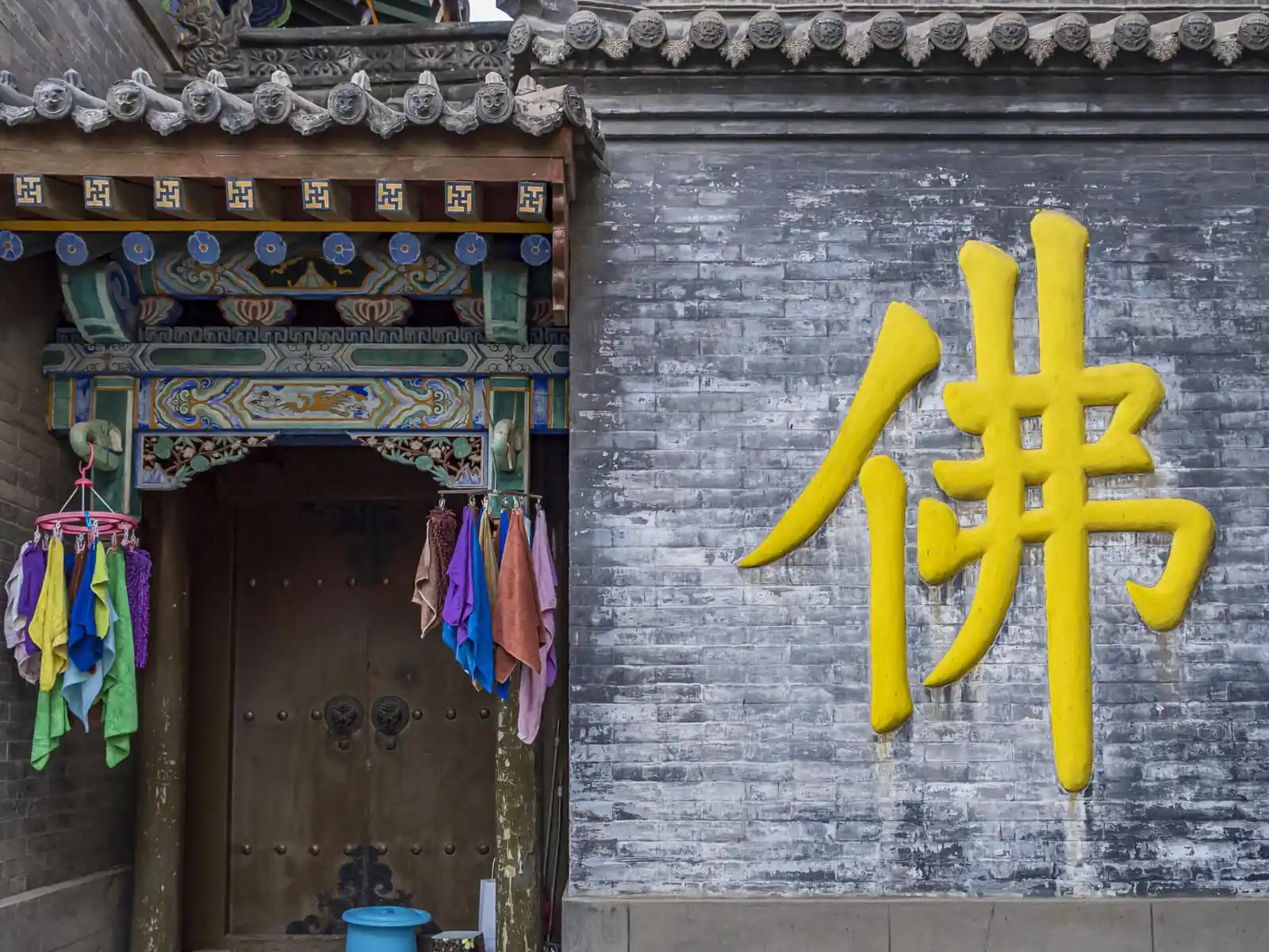 Pushou Temple, Mount Wutai, shanxi, china, china tour, Bright yellow Chinese character painted on a weathered gray brick wall beside a richly painted temple doorway with hanging colorful cloths.