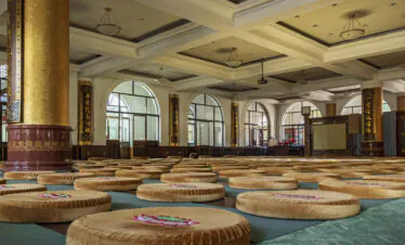 Pushou Temple, Mount Wutai, shanxi, china, china tour, Large hall with rows of round floor cushions on green mats, tall gold pillars with Chinese inscriptions, and arched windows in the background.