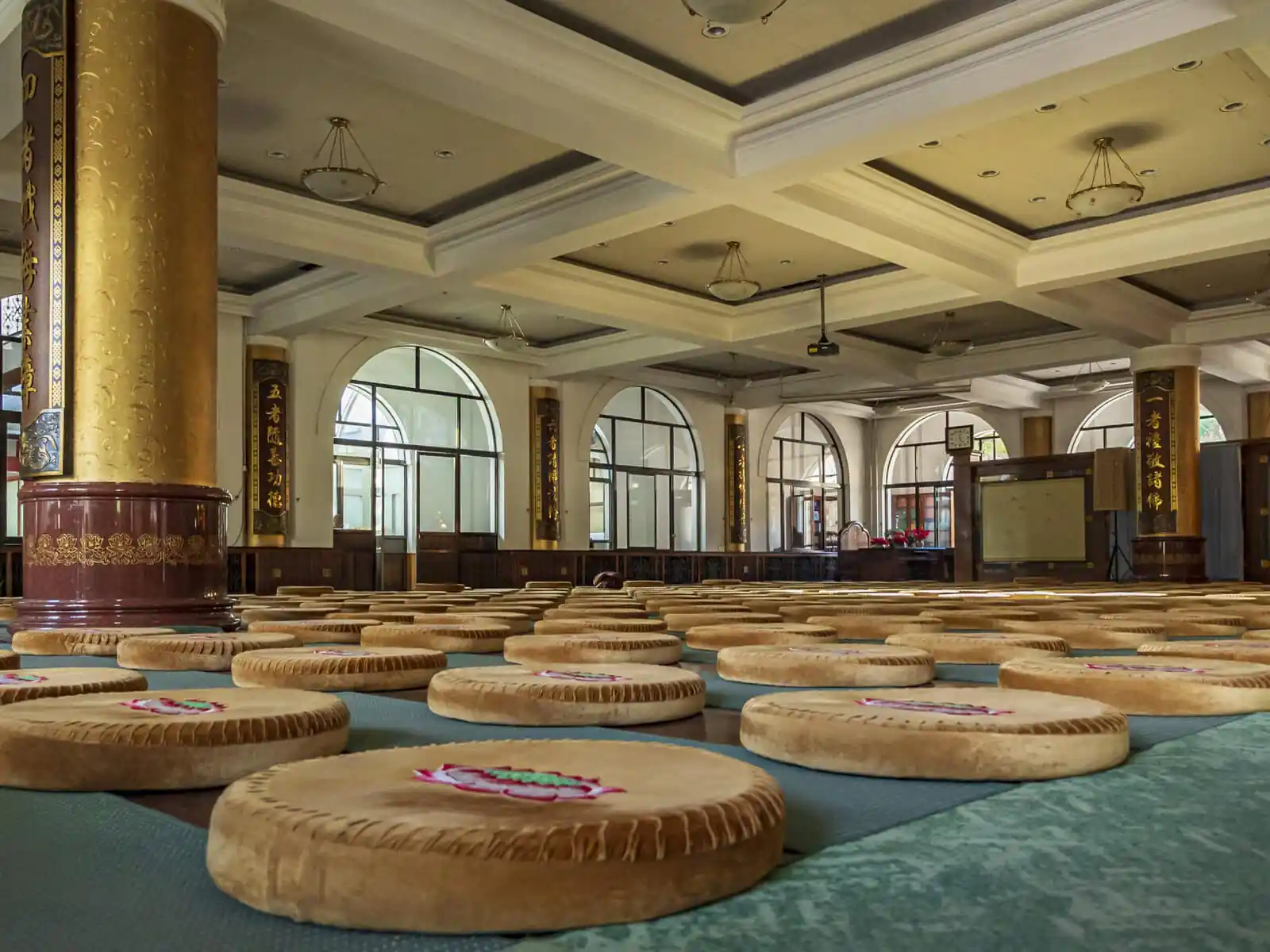Pushou Temple, Mount Wutai, shanxi, china, china tour, Large hall with rows of round floor cushions on green mats, tall gold pillars with Chinese inscriptions, and arched windows in the background.