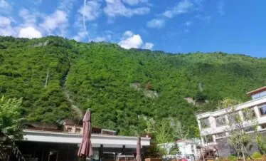 Hot Spring, Bipenggou, 3-Days Explore Western Sichuan in Winter- Siguniang Mountain, Bipenggou, and Dagu Glacier, china tour, Lakeside resort with a wooden deck, brown umbrellas, and lounge chairs by calm water, set against green mountains under a blue sky with scattered clouds