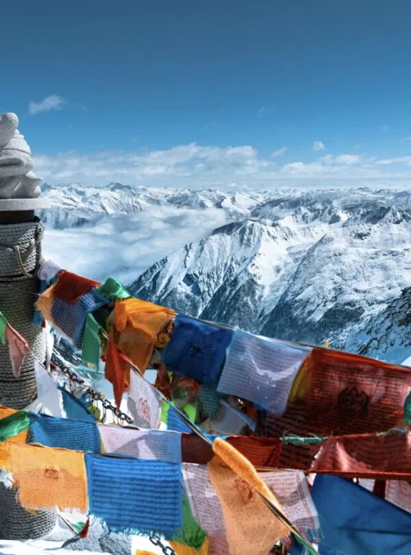 Bipenggou, 3-Days Explore Western Sichuan in Winter- Siguniang Mountain, Bipenggou, and Dagu Glacier, china tour, Colorful prayer flags flutter around a stone cairn atop a snowy mountain, with a vast range of snowcapped peaks in the background.