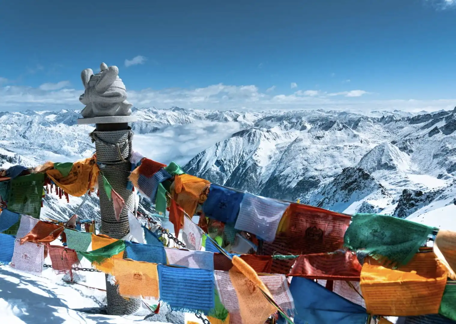 Bipenggou, 3-Days Explore Western Sichuan in Winter- Siguniang Mountain, Bipenggou, and Dagu Glacier, china tour, Colorful prayer flags flutter around a stone cairn atop a snowy mountain, with a vast range of snowcapped peaks in the background.