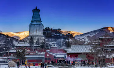 Snow-dusted White Pagoda under a Golden Mountain Sunrise, Mount Wutai, shanxi, china, china tour, Snow-covered temple complex with a towering white stupa in the foreground and snow-dusted rooftops, set against sunlit hills at dusk.