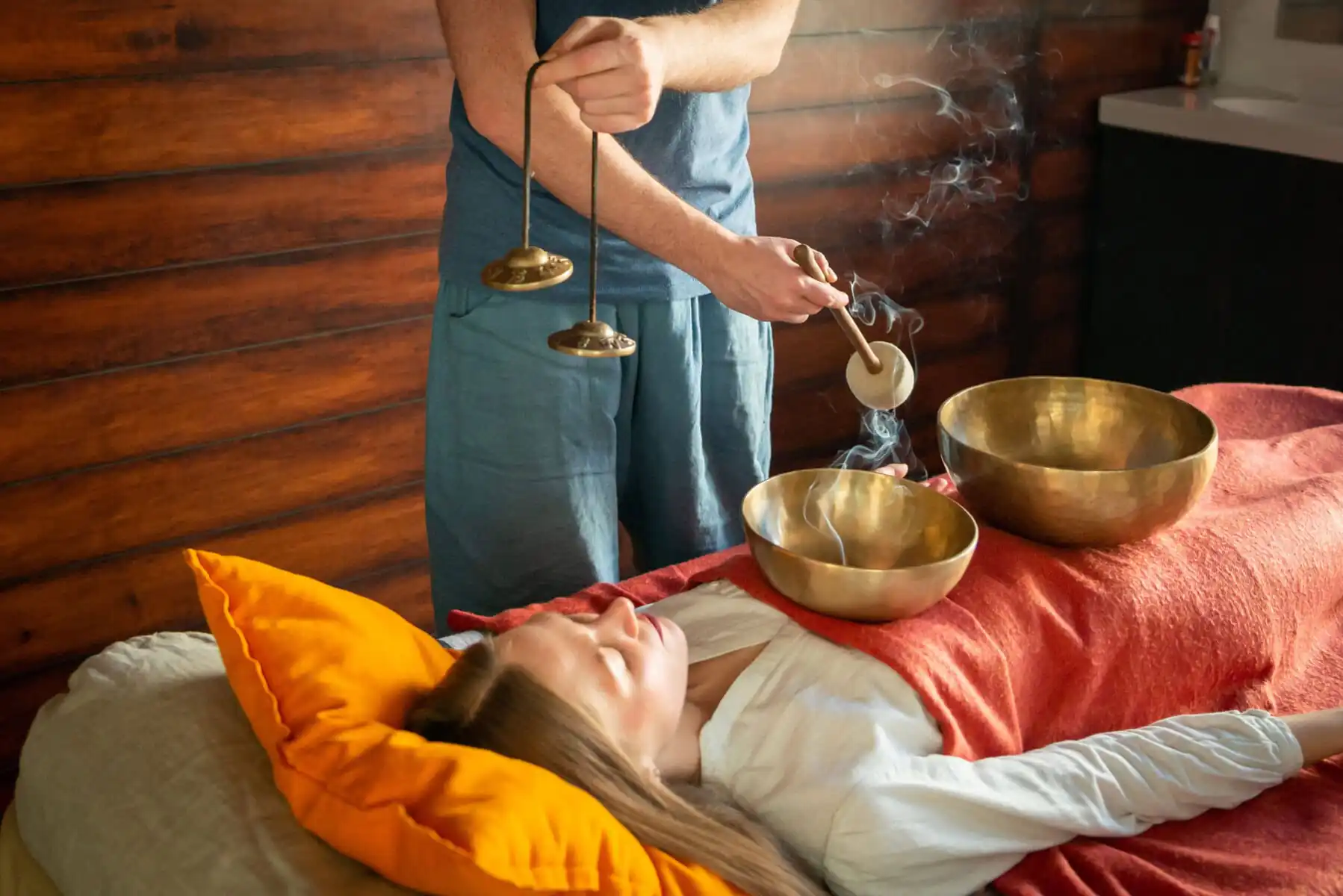 Tibetan singing bowls treatment in spa salon, Mount Wutai, shanxi, china, china tour, Person lying on a bed with orange pillow, eyes closed, as a practitioner plays brass singing bowls for sound therapy.