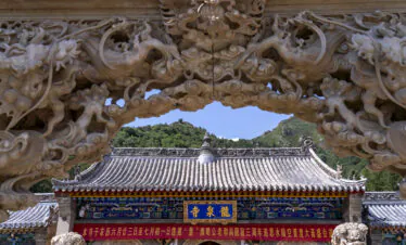 Longquan Temple, Mount Wutai, shanxi, china, china tour, Ornate stone dragon archway framing a temple roof with mountains in the background