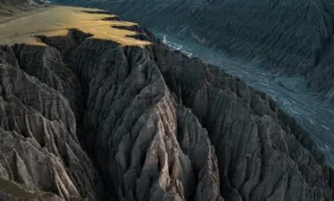 north xinjiang, western china, china tour, Jagged canyon walls with deep grooves and a grassy plateau at the top, distant mountains under a cloudy sky