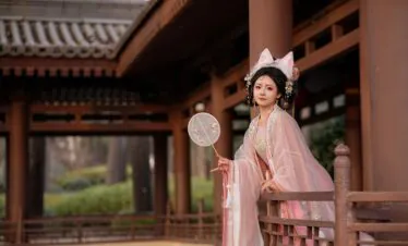 hanfu photoshoot, xi'an, female, solo, china tour, Woman in pale pink traditional attire with floral headpiece standing on a wooden veranda, holding a round embroidered fan.