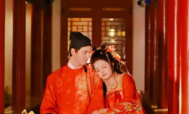 hanfu photoshoot, xingqing palace, xi'an, tang dynasty, couple, chinatravel, Couple in red traditional Chinese wedding attire sitting together in a decorated corridor, heads resting on each other under colorful beams in a temple setting.