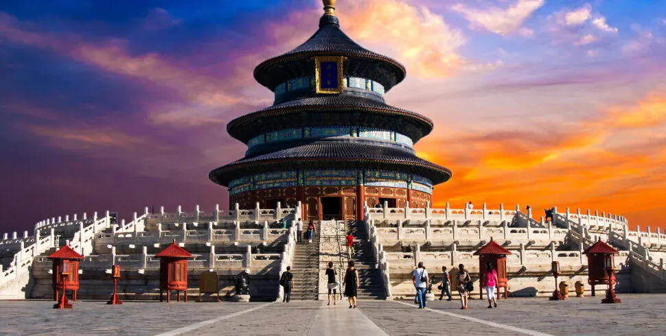 Beijing's Temple of Heaven, chinaexplorertour, Beijing's Temple of Heaven at sunset: a circular, multi-tiered pavilion atop white marble stairs with visitors approaching against a orange-purple sky.