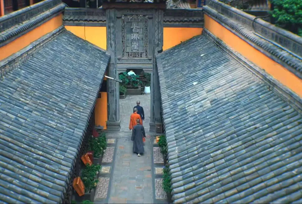 Luohan Temple in Chongqing, chinaexplorertour, Courtyard path between orange walls and sloped tiled roofs, monks walking toward a carved gate at a temple entrance