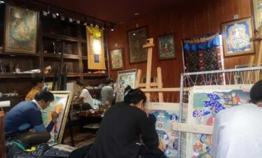 Western Sichuan, Sichuan Tibetan area, china, chinaexplorertour, Artists gathered in a wood-paneled studio, painting vibrant Buddhist thangka-style artworks on easels and scrolls around a cozy workshop space