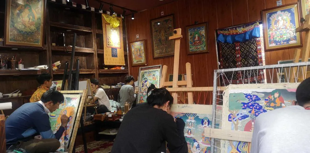 Western Sichuan, Sichuan Tibetan area, china, chinaexplorertour, Artists gathered in a wood-paneled studio, painting vibrant Buddhist thangka-style artworks on easels and scrolls around a cozy workshop space