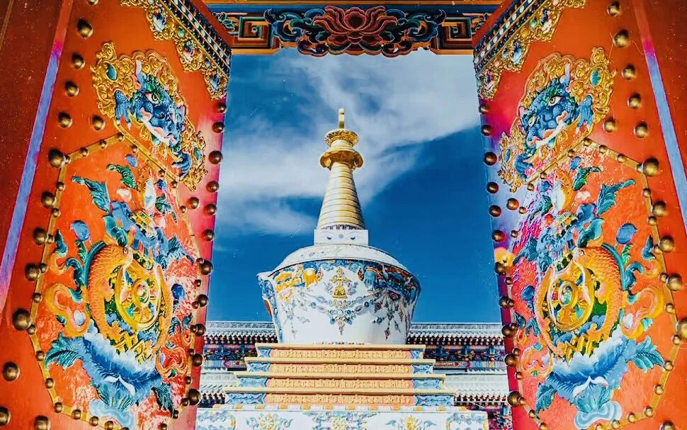 wutai mountain, shanxi, chinaexplorertour, Colorful ornate temple gate opening to a white-and-gold stupa under a bright blue sky, with dragon motifs on red pillars.