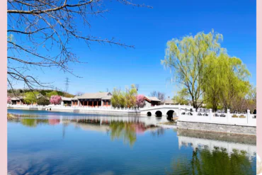 beijing, china, chinaexplorertour, Tranquil lake with a white arched bridge and traditional buildings along the shore, reflected in the water.