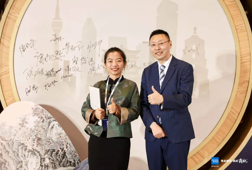 china explorer tour, china travel agency, china tour, Two professionals pose with thumbs up in front of a round backdrop featuring a city skyline and signatures.