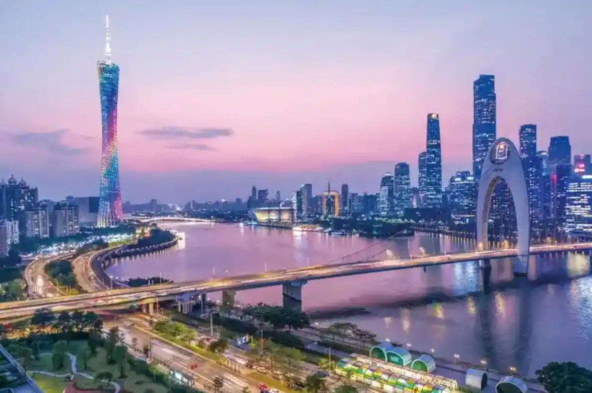 guangzhou, china, chinaexplorertour, A nighttime city skyline with a colorful-lit tower, a curved arch bridge over a river, and bright high-rise buildings reflecting on the water.
