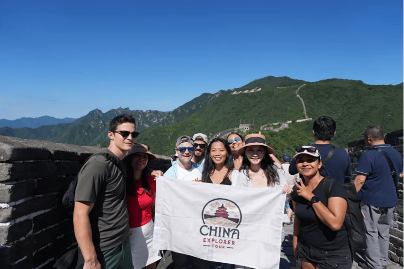 the great wall, beijing, chinatravel, Group of tourists posing with a China Explorer Tour banner on the Great Wall, mountains in the background and blue sky above.