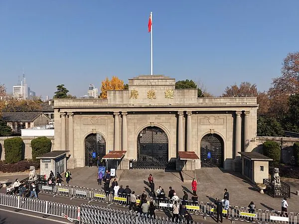 nanjing presidental palace, jiangsu, chinatrip, Stone gate with three arches and a Chinese flag flying atop, people queuing behind barricades in front of the entrance.
