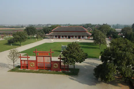the capital of zheng and han states, xinzheng, henan, Aerial view of a historic Chinese courtyard with a red gate, green lawn, and a large traditional building in the distance at a cultural site.