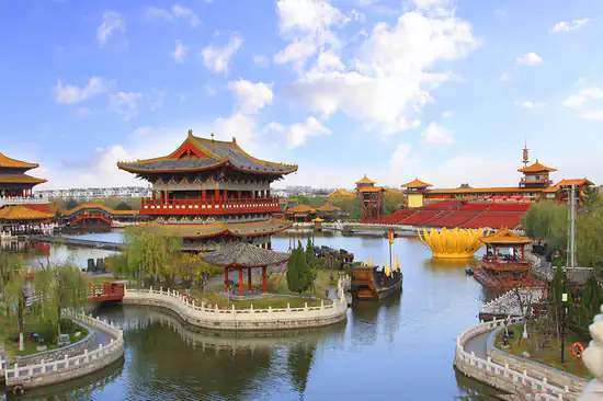 qingming river park, kaifeng, henan, chinatrip, Traditional Chinese pagoda-style buildings sit on an interconnected lakeshore, linked by white stone bridges under a blue sky.