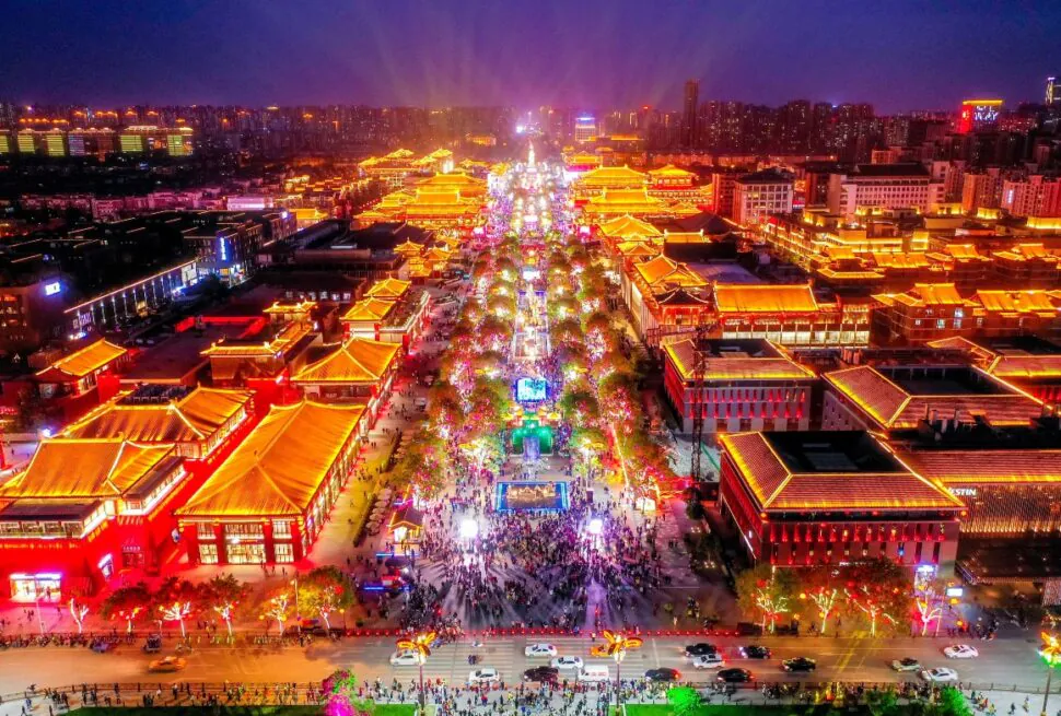 flaming mountains, turpan, xinjiang, china tour, Aerial night view of a crowded festival along a bright, lantern-lit avenue flanked by traditional Chinese pagodas and buildings.
