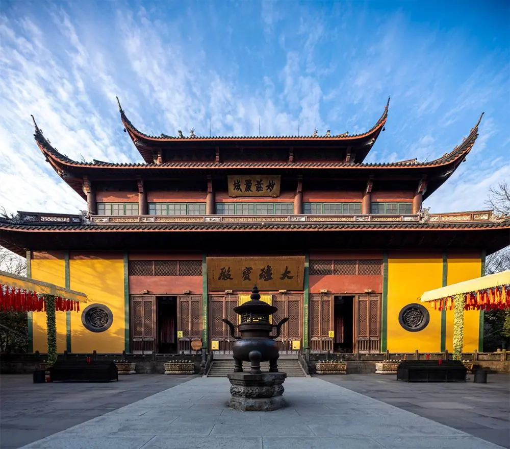 Lingyin Temple, hangzhou, zhejiang, china tour, Traditional Chinese temple with yellow walls and curved roofs, central incense burner in a stone courtyard under a blue sky