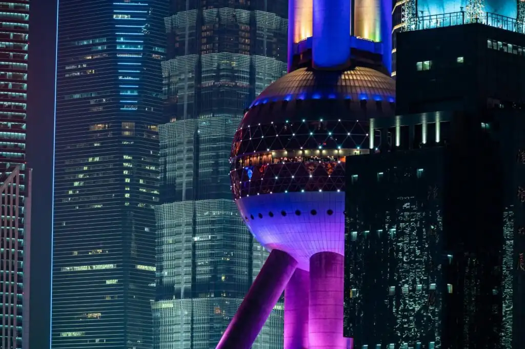 shanghai, chinatrip Nighttime cityscape featuring the illuminated Oriental Pearl Tower beside tall glass skyscrapers in Shanghai.