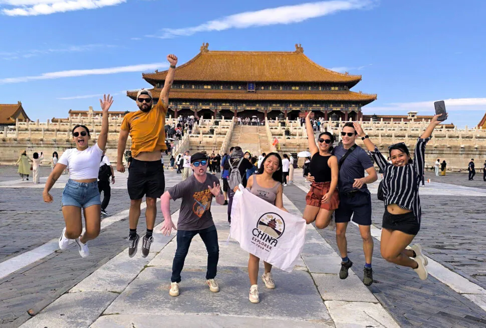 the forbidden city, beijing, chinatrip, Group of seven tourists mid-jump in front of a yellow-roofed imperial hall; one holds a China Explorer Tour banner.