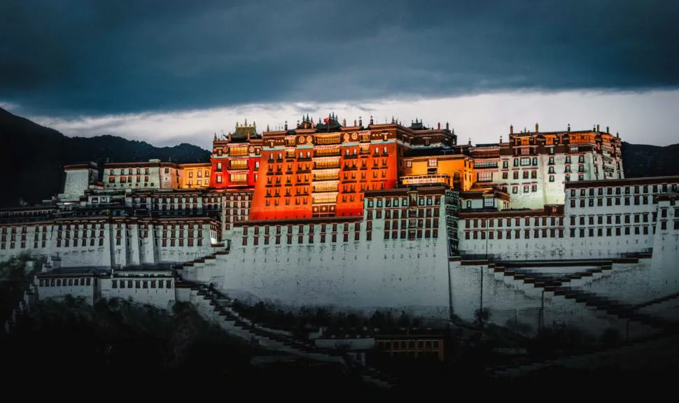 potala palace, tibet, chinatrip, Potala Palace, a large white-and-red Tibetan fortress atop a hill against a dark sky at dusk.