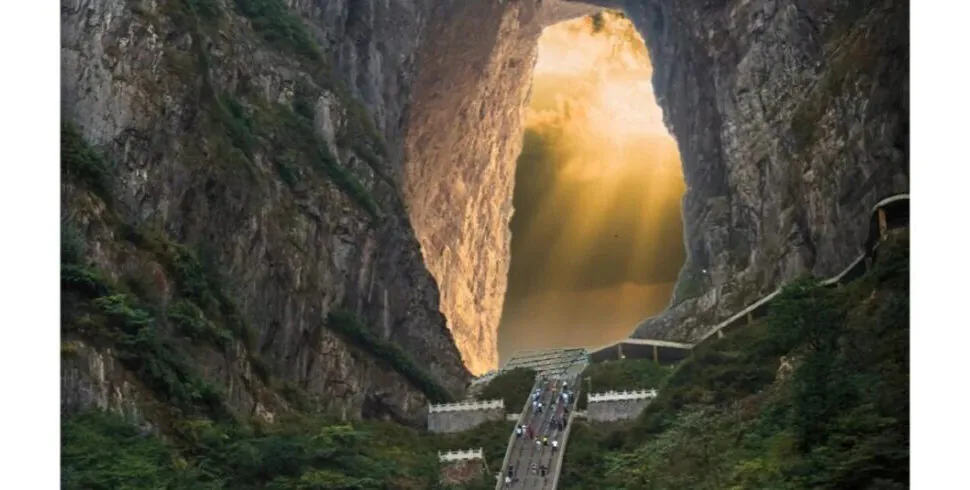 tianmen mountain, zhangjiajie, chinatrip, Bridge spanning a steep valley through a massive rock arch, with sunlight pouring through the opening and people walking along the path below.