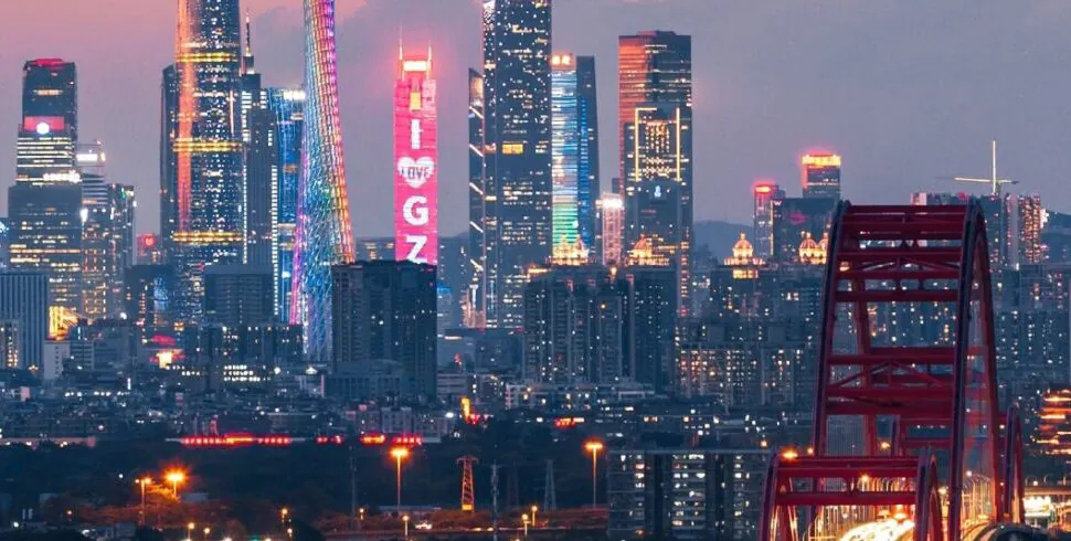 guangzhou, chinatrip, Nighttime city skyline with illuminated skyscrapers and a red bridge in the foreground.