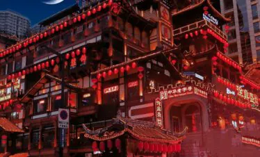 hongya cava, chongqing, china tour, Night panorama of a multi-tiered traditional Chinese building lit with red lanterns and neon signs, crescent moon in dark sky, busy street below with taxis and scooters.
