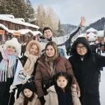Harbin Trip, heilongjiang, china tour, Group of friends smiling and waving in a snowy village street with wooden shops and red lanterns.